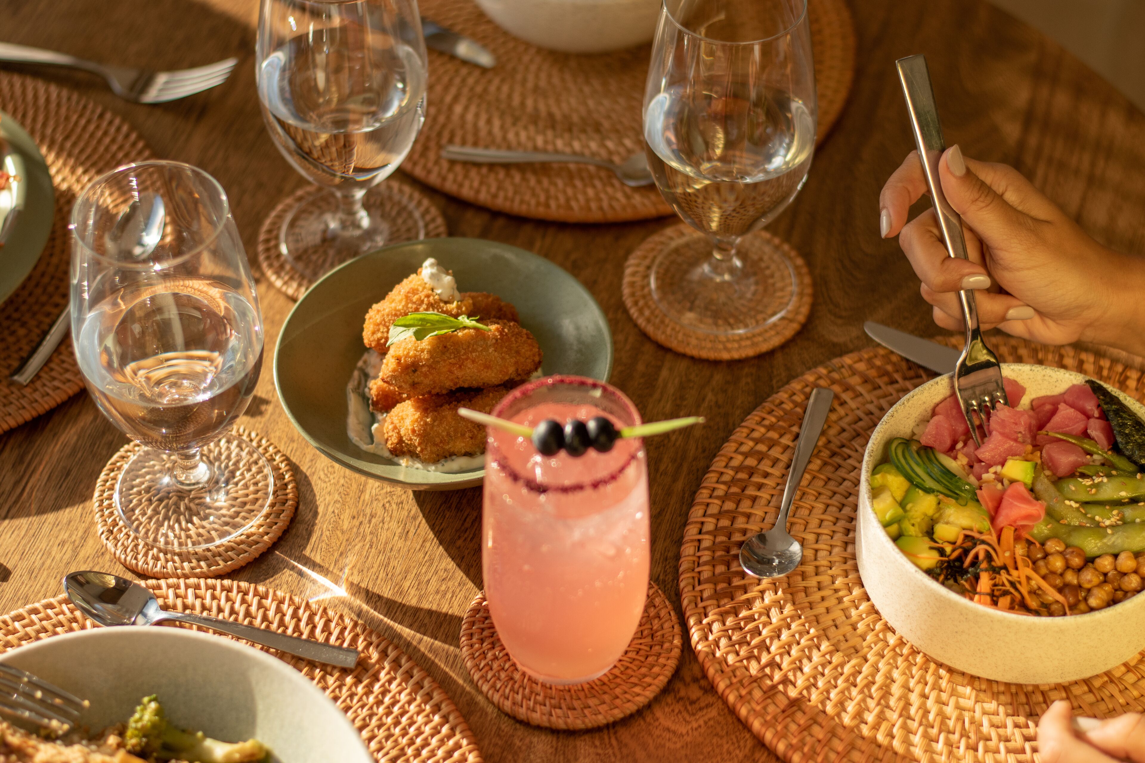 A table set with various dishes, including a bowl of salad, a glass of pink drink, and a plate of breaded food.
