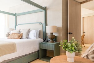 Una habitación de hotel ordenada con una cama, una mesita de noche con lámpara, una planta pequeña y una silla.