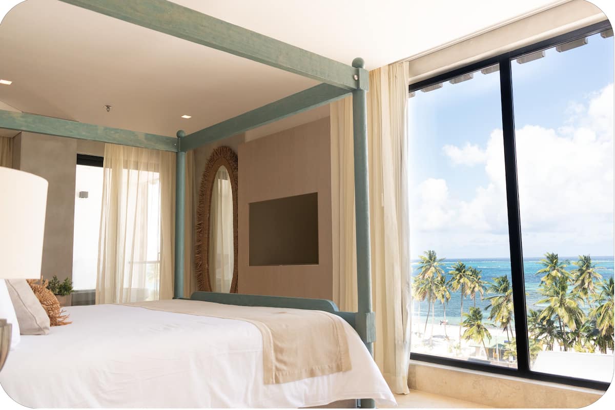 Ein Schlafzimmer mit großem Fenster und Blick auf einen Strand, einem Bett und einem Spiegel.