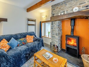 A living room with a stone fireplace, a sofa with patterned cushions, a coffee table with a book and a bowl, and a wicker chair.