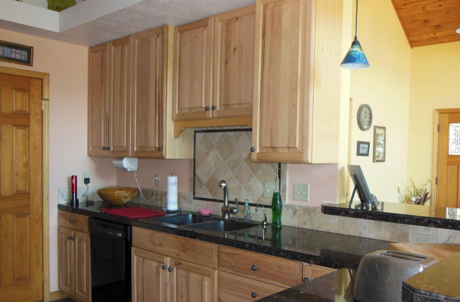 A kitchen with wooden cabinets, a black countertop, a sink, a toaster, and a hanging light fixture.