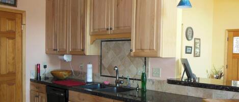 A kitchen with wooden cabinets, a black countertop, a sink, a toaster, and a hanging light fixture.
