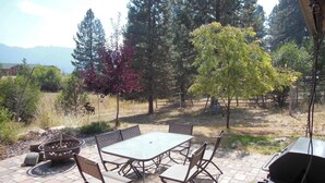 Une terrasse extérieure avec une table et des chaises, entourée d’arbres et offrant une vue sur la montagne.