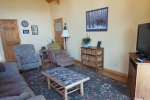 A living room with a sofa, armchair, coffee table, TV stand, and a painting on the wall.