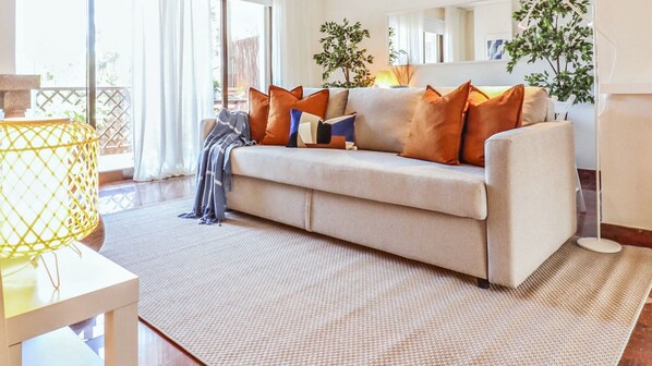 A modern living room with a beige sofa, multiple cushions, a woven rug, and a yellow lamp.