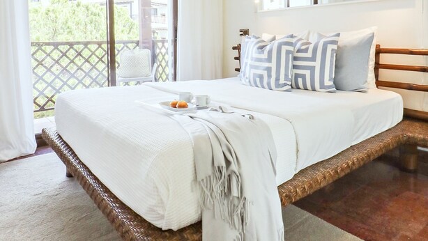 A bedroom with a large bed, white bedding, a tray with pastries, and a view of greenery outside.