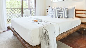 A bedroom with a large bed, white bedding, a tray with pastries, and a view of greenery outside.