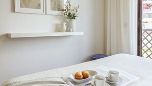 A neatly arranged breakfast tray with muffins and cups on a bed, a white shelf with decorative items, and a view of a balcony with a lattice railing.