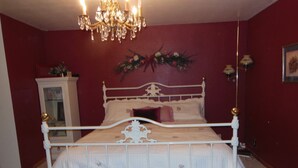 A bedroom with a white metal bed frame, a chandelier, and a red wall. - ATV/Snowmobiler's Paradise - Ride Out from the Cabin for Miles on End! (Placerville)