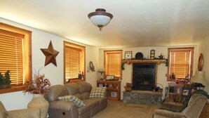 A cozy living room with a fireplace, a star decoration on the wall, and a ceiling fan. - ATV/Snowmobiler's Paradise - Ride Out from the Cabin for Miles on End! (Placerville)