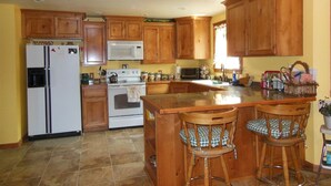 A kitchen with wooden cabinets, a refrigerator, a microwave, a stove, and two bar stools. - ATV/Snowmobiler's Paradise - Ride Out from the Cabin for Miles on End! (Placerville)