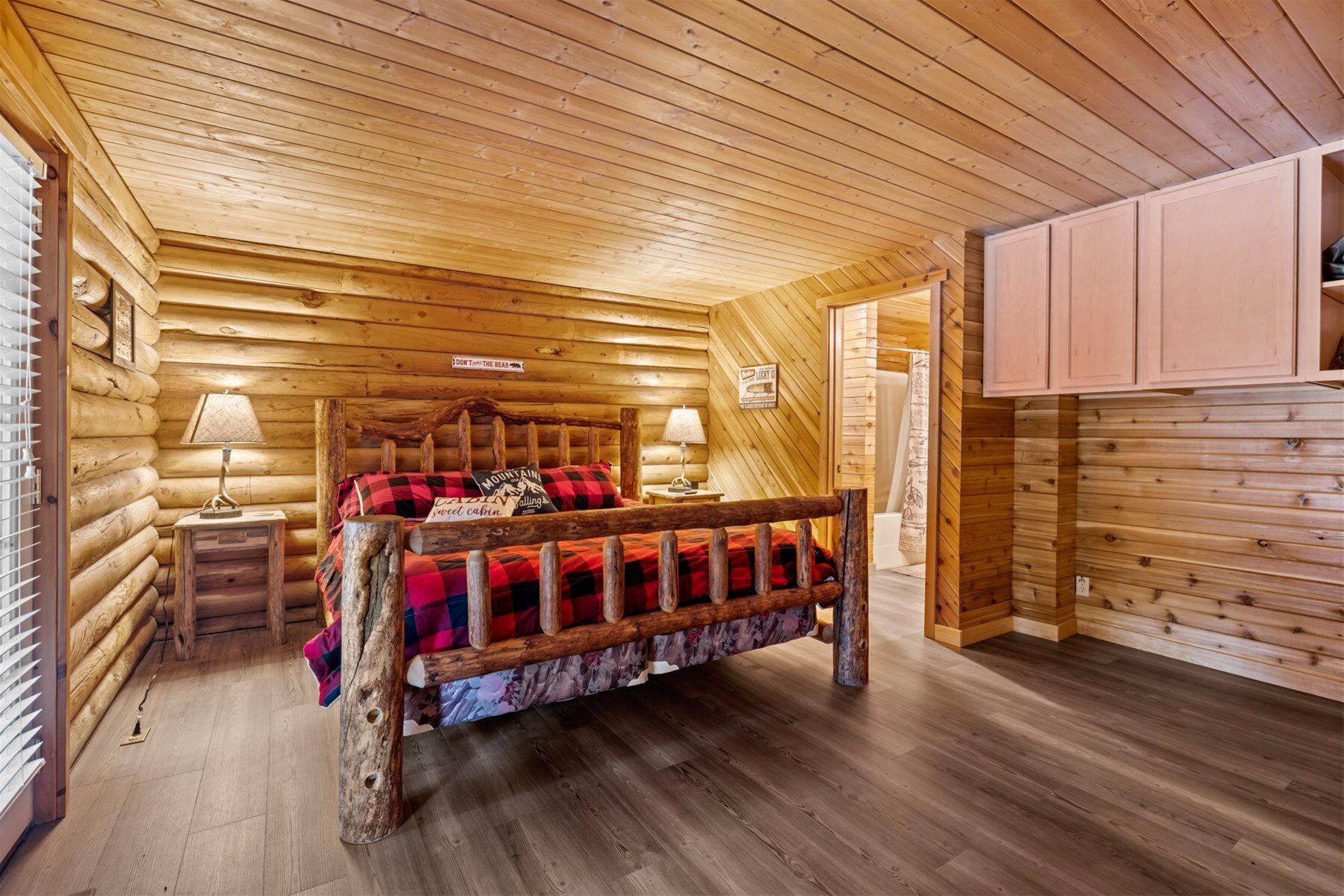 Un dormitorio tipo cabaña de madera con una cama de madera, dos mesitas de noche, un tocador y un armario de madera.