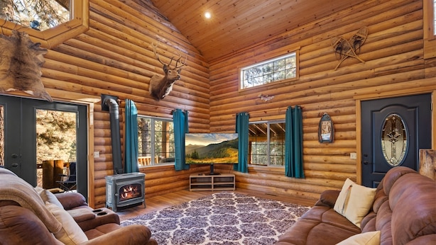 A log cabin interior with a fireplace, leather couches, and a scenic mountain view through the windows.