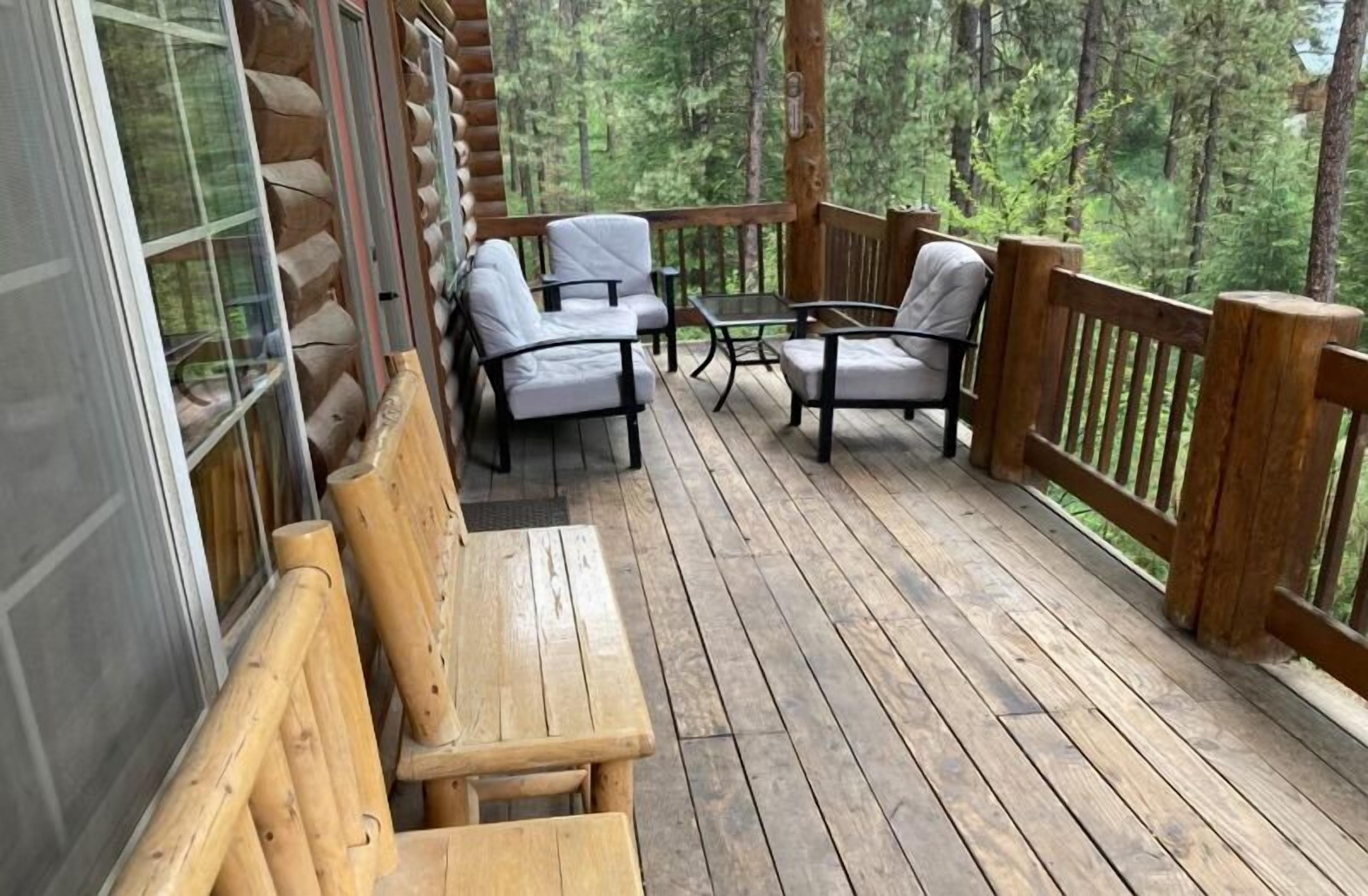A wooden deck with a table and chairs, surrounded by a wooden railing, overlooking a forested area.