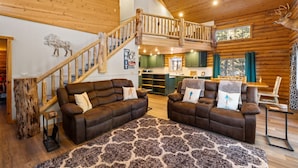 A spacious living area with two brown leather sofas, a wooden staircase, and a view of the kitchen and dining area.
