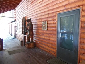 Una cabaña de madera con una estatua de oso sobre un tocón, una puerta y un banco en el exterior.