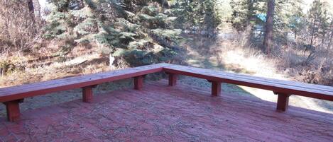 Un banc en bois avec un dossier rouge et un sol en briques, entouré d’arbres.