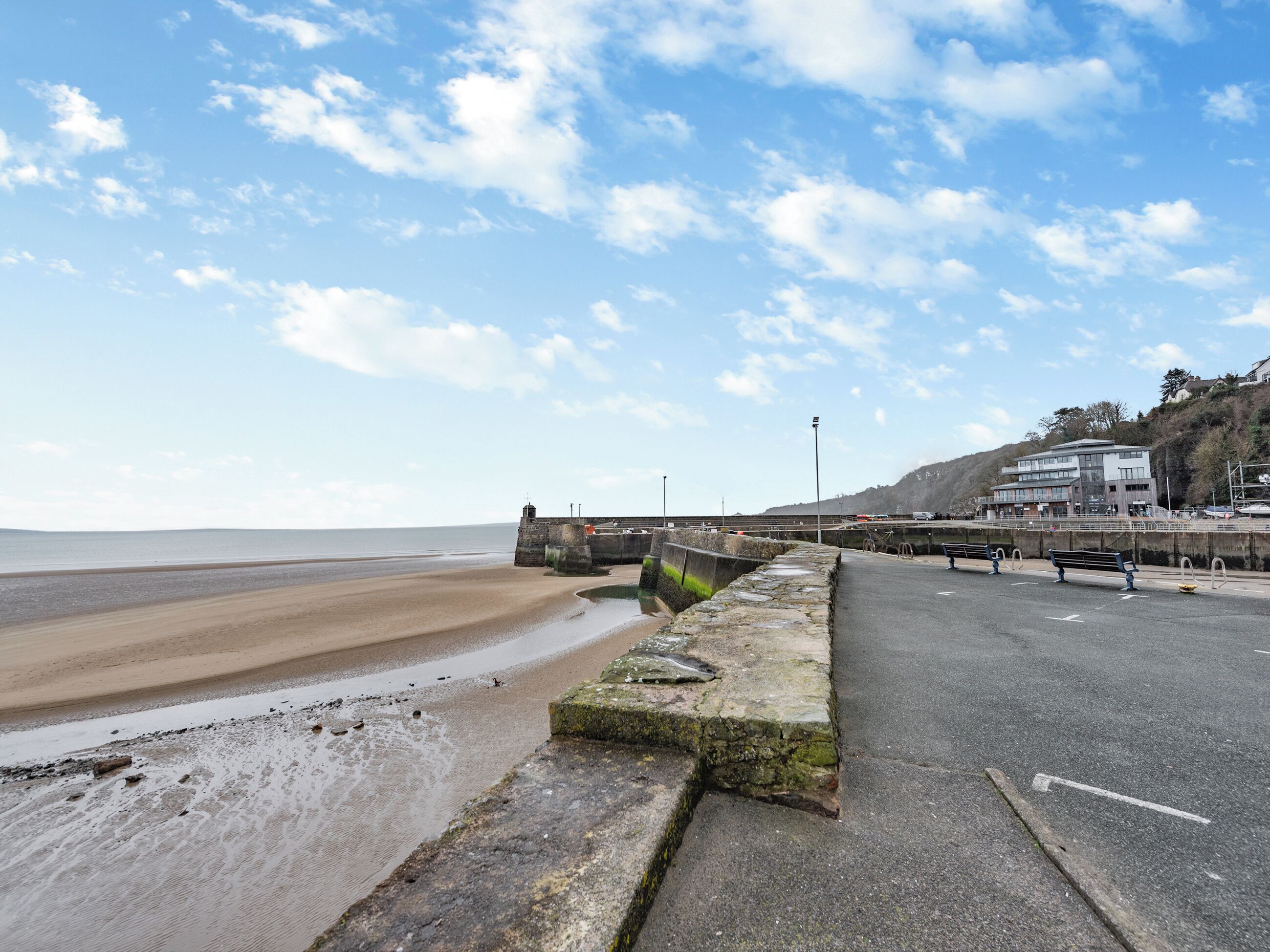 A coastal road with a beach on one side and a building complex on the other.