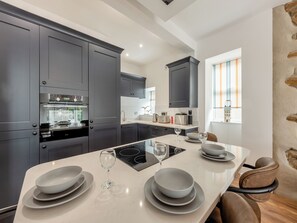 A modern kitchen with dark cabinets, a central island, and a dining area with chairs. - Sandy View - UK43056 (Saundersfoot)