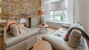 Un salon avec un mur en pierre, une cheminée, deux canapés, une table basse ronde et une grande fenêtre donnant sur un beau paysage.