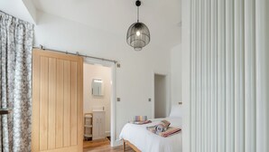 Une chambre avec une armoire en bois, un lit avec une literie à rayures, un luminaire suspendu et une porte blanche.