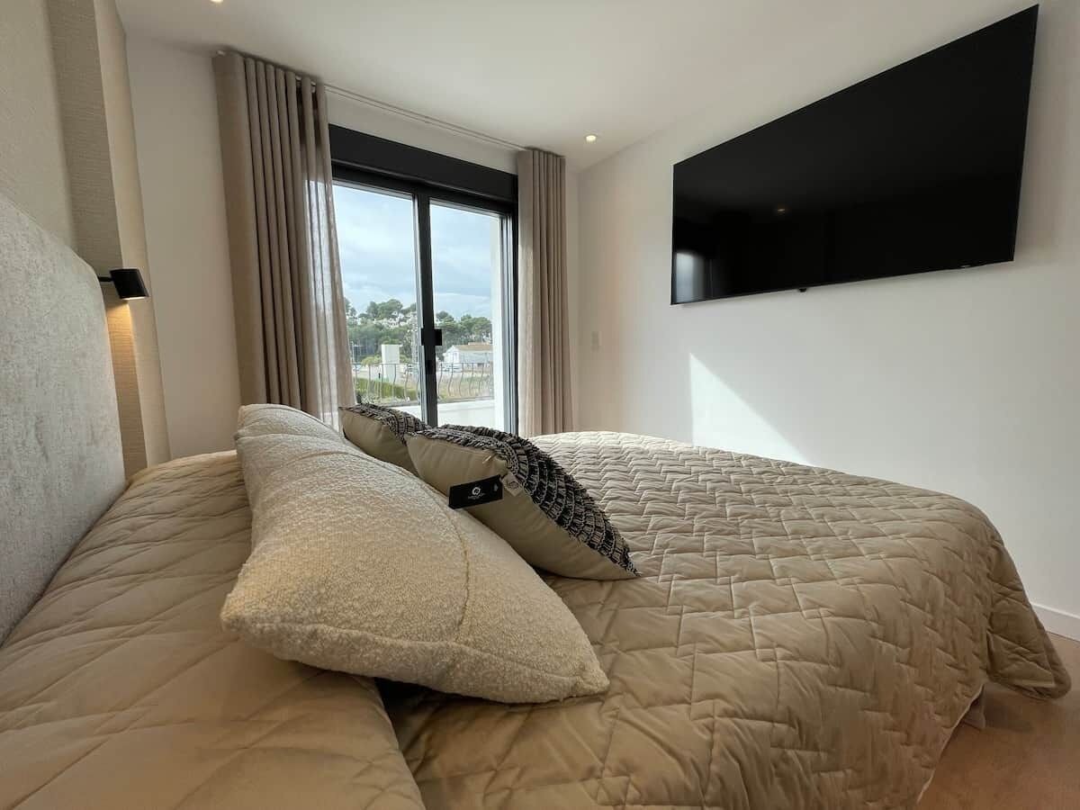 Una camera da letto con un letto, una televisione a schermo piatto montata a parete e una finestra con tende.