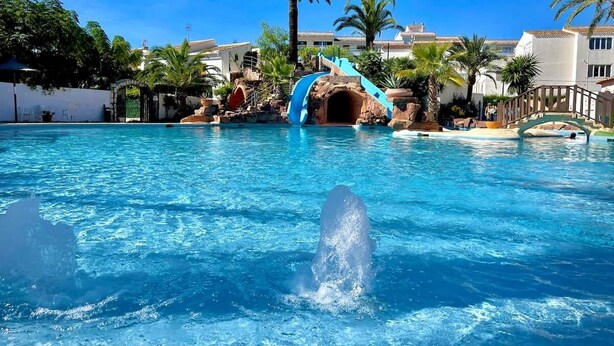 A swimming pool with a water slide and palm trees.