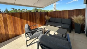 An outdoor patio with a wooden fence, a grey sofa, and two armchairs.