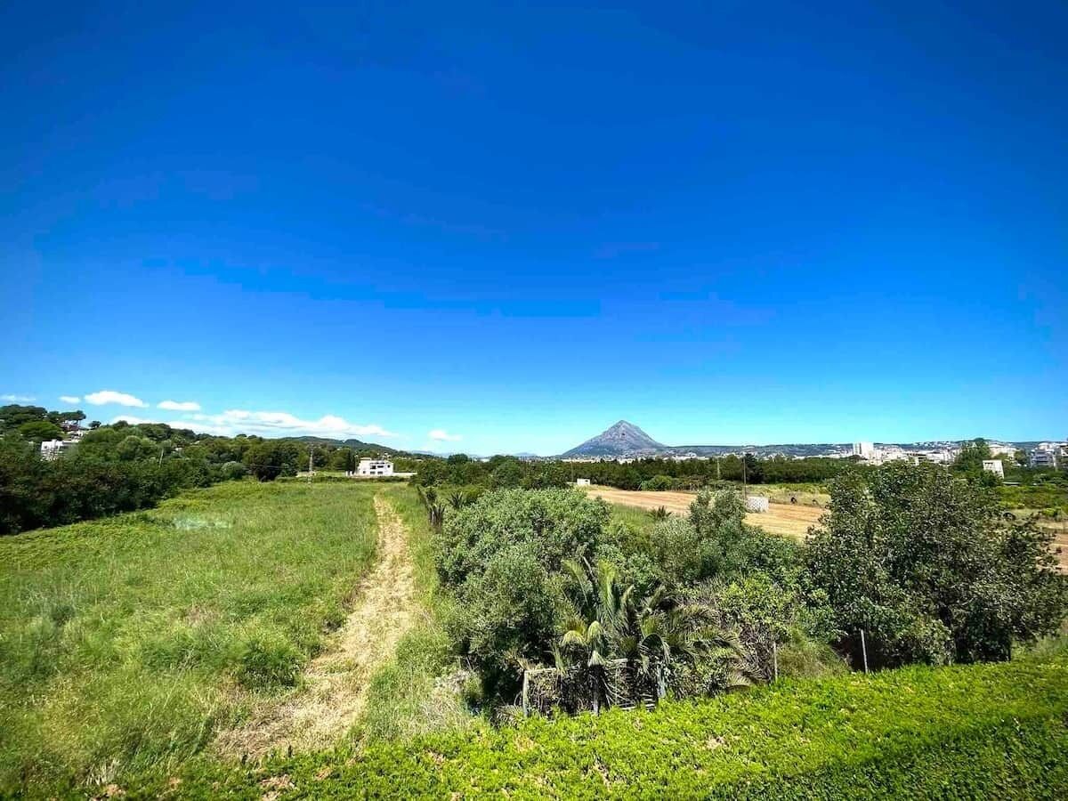 Un paysage rural avec un ciel dégagé, un sentier menant à une maison et une montagne à l’horizon.
