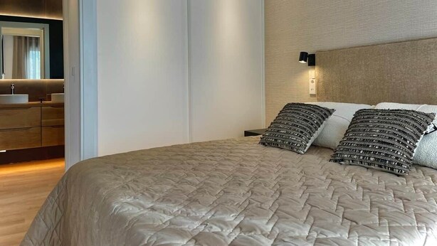 A bedroom with a large bed, a wardrobe, a bedside table, and a wall-mounted light.