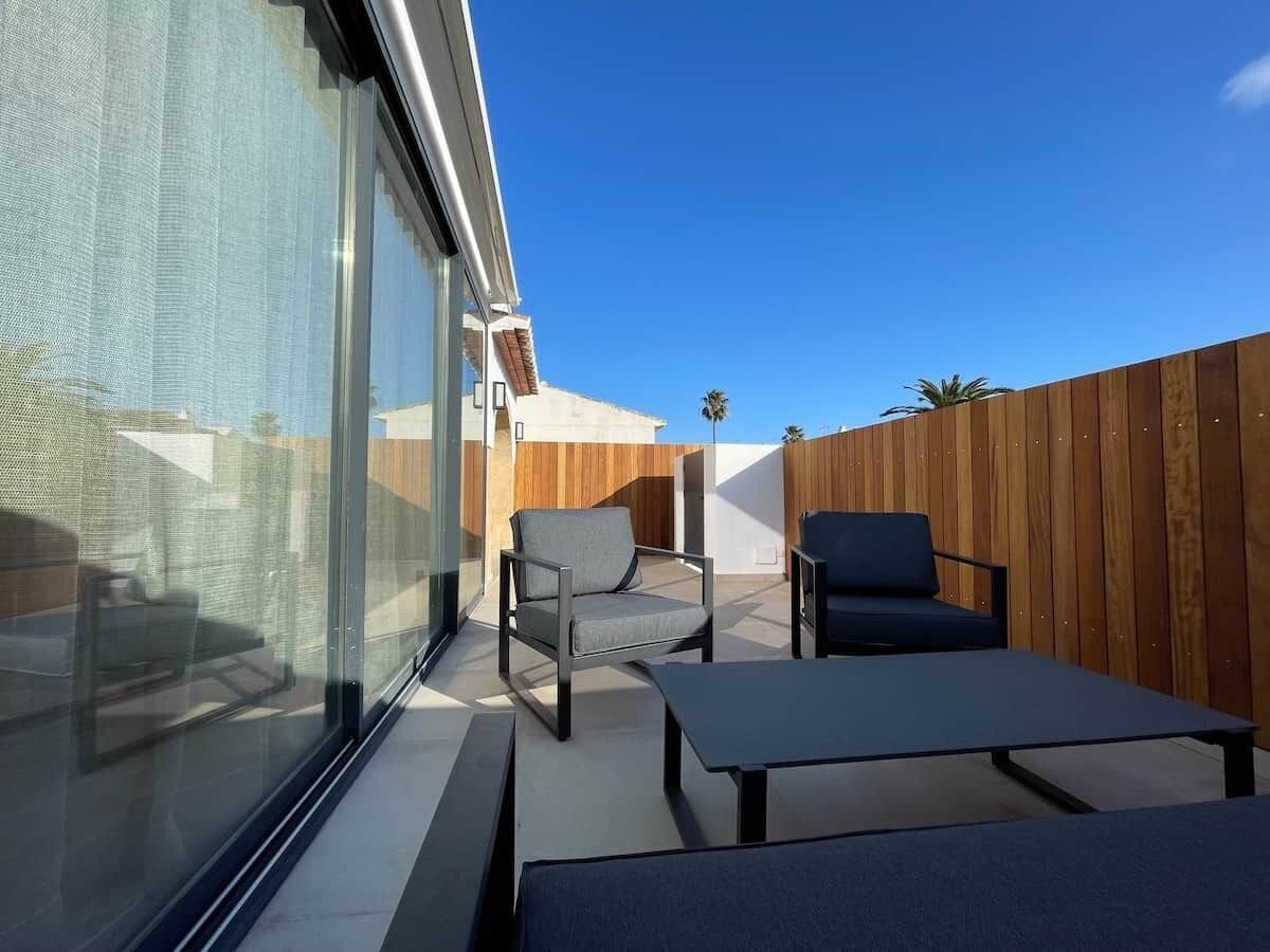 Eine moderne Außenpatio mit Glaswand, Holzzaun und zwei Lounge-Stühlen.