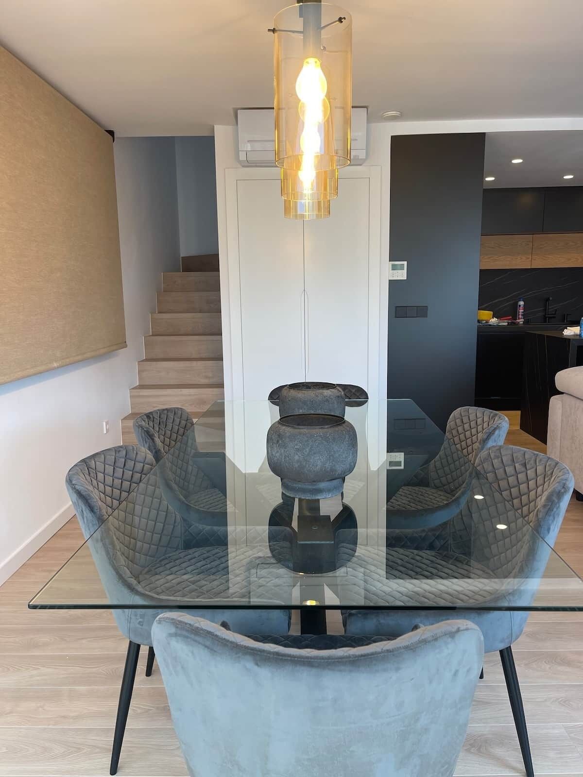 Een moderne eetruimte met een glazen tafel, beklede stoelen, een opvallend middelpunt en een trap op de achtergrond.