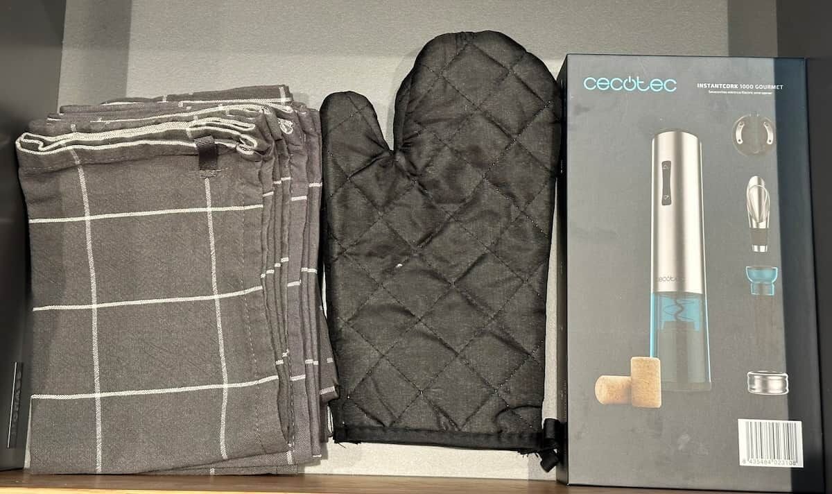 Ein Stapel gefalteter Handtücher und ein schwarzer Topflappen neben einer Kiste mit der Aufschrift 'cecotec InstantCork 1000 Gourmet'.