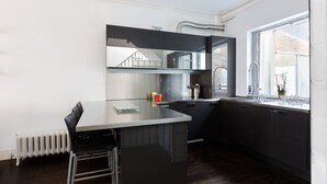 A modern kitchen with a central island, dark cabinetry, and a window providing natural light. - Stunning flat in Notting Hill, Portobello (London)