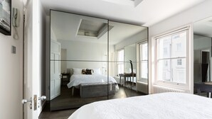 A modern bedroom with a large bed, a mirrored wardrobe, and a view of the city through a window. - Stunning flat in Notting Hill, Portobello (London)