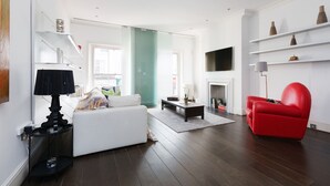 A modern living room with a white sofa, a red armchair, a coffee table, and a TV mounted on the wall. - Stunning flat in Notting Hill, Portobello (London)