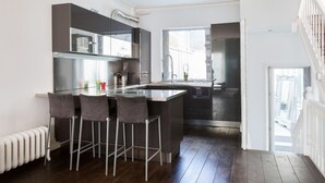 A modern kitchen with a central island, bar stools, a stainless steel refrigerator, and a window providing natural light. - Stunning flat in Notting Hill, Portobello (London)
