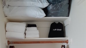 A closet with neatly folded towels, a hair dryer, and a robe hanging.