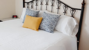 A neatly made bed with a white duvet, two patterned pillows, and a single solid yellow pillow.