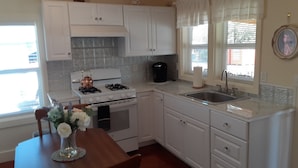 A kitchen with white cabinets, a stove, a sink, and a window with curtains.
