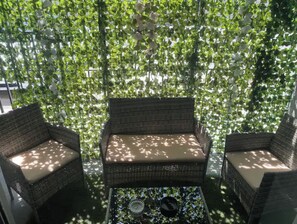 Relax in a serene outdoor space surrounded by lush greenery, featuring a wicker bench and chairs with cushioned seats.