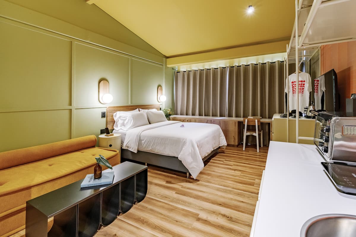 A hotel room with a bed, a desk, a chair, a small table, and a mirror.