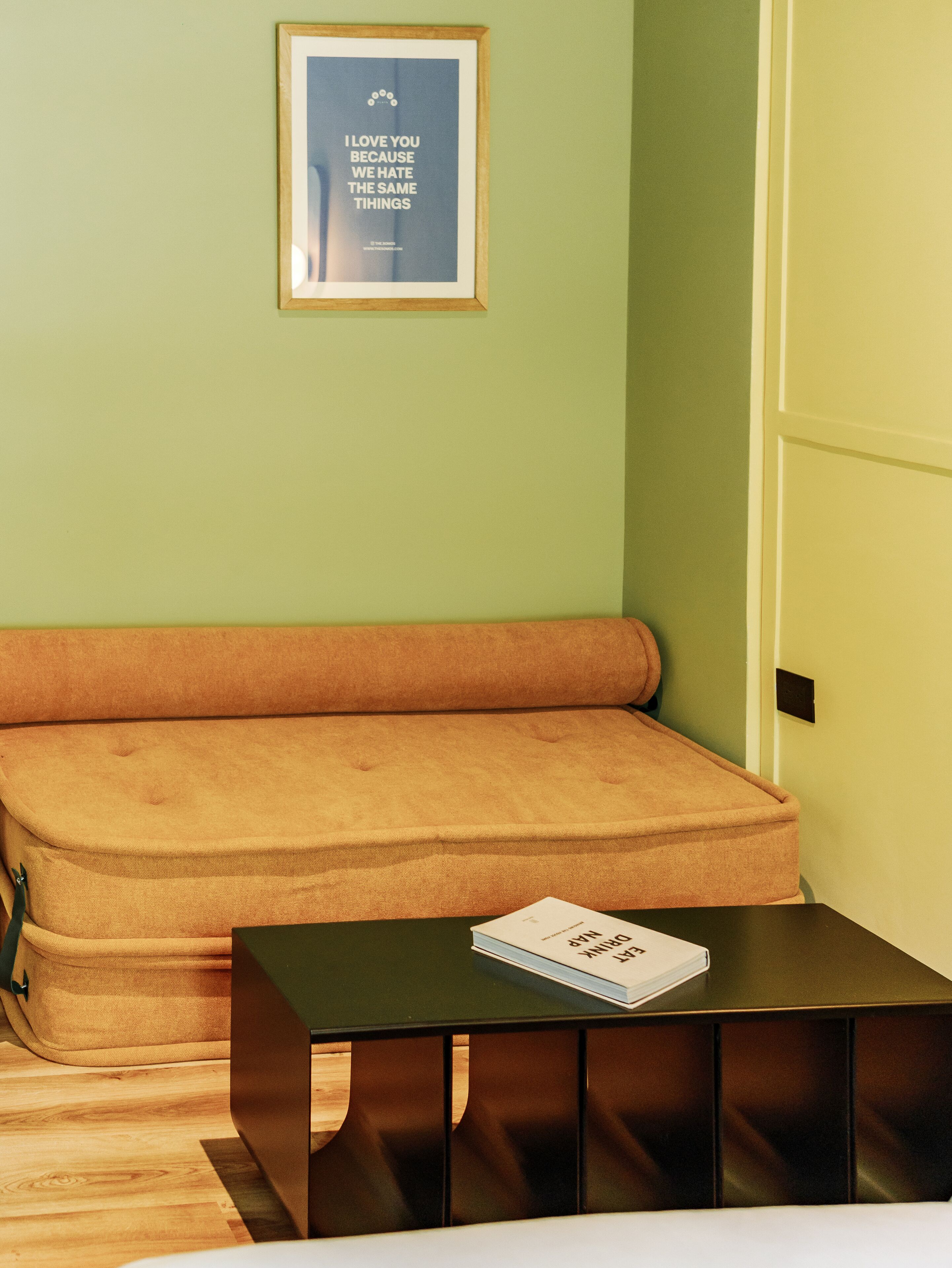 A room with a beige sofa, a black table with a book, and a framed quote on the wall.