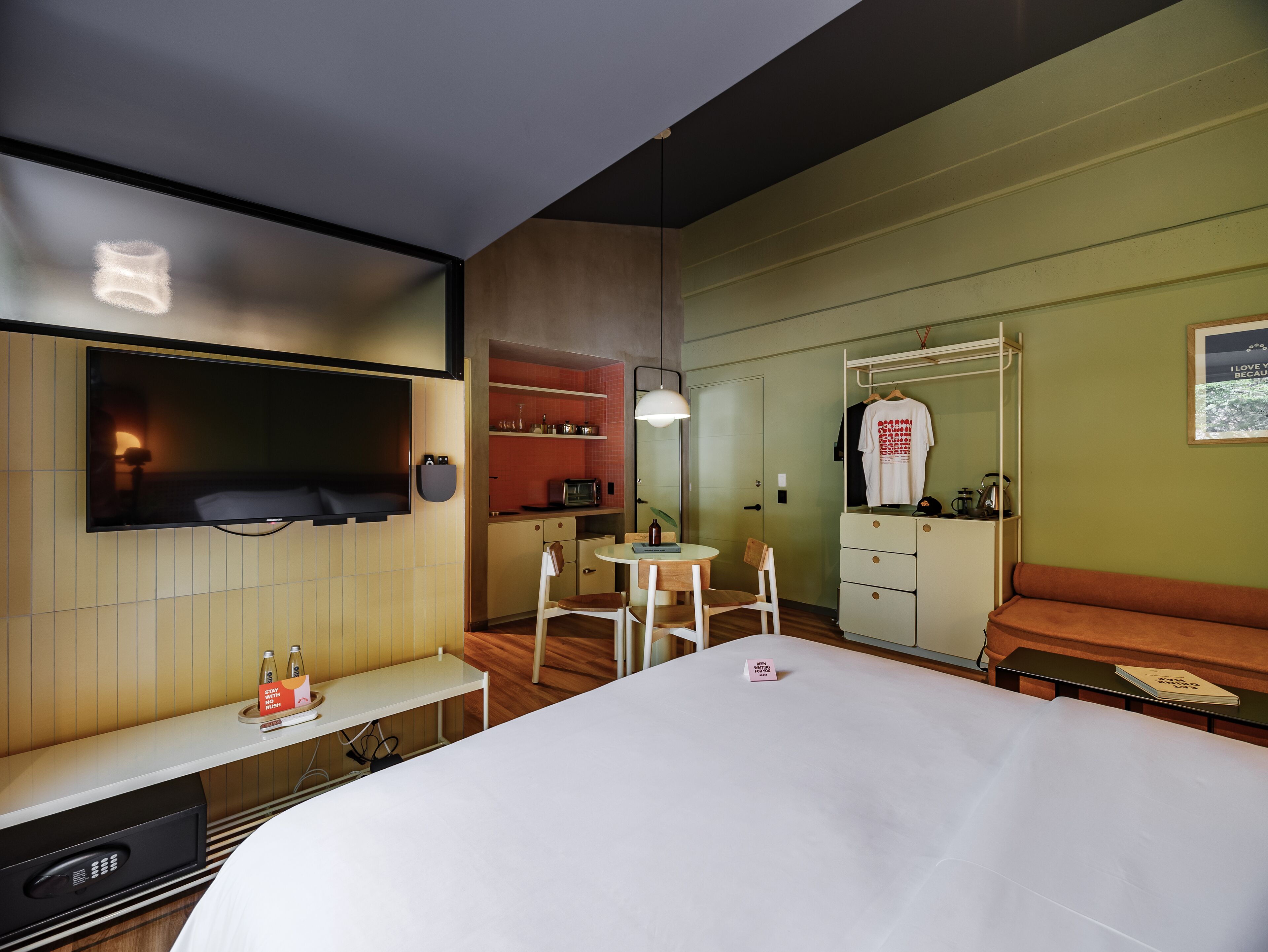 A hotel room with a bed, a TV mounted on the wall, a small kitchenette, a seating area with a table and chairs, and a sofa.