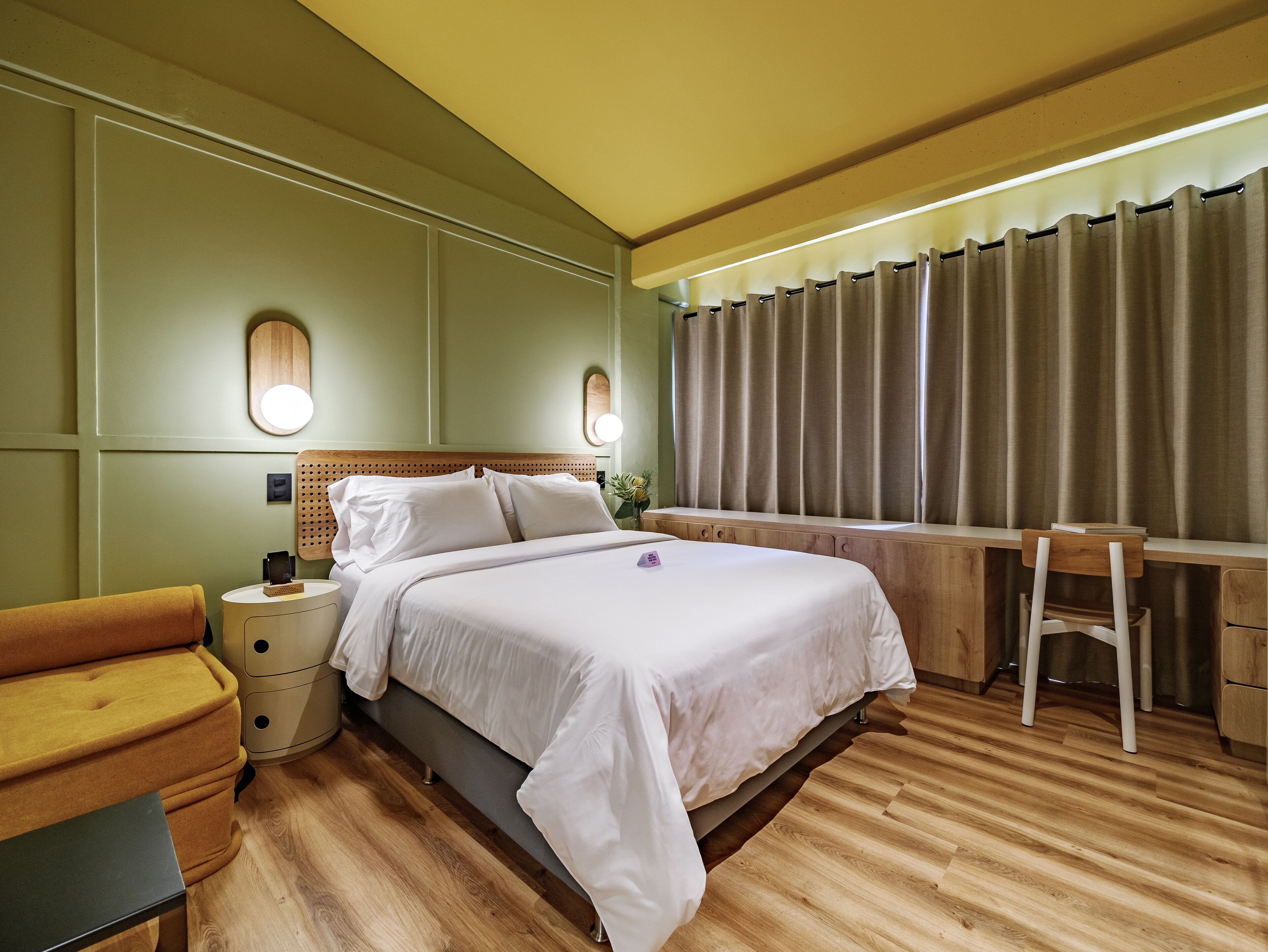 Quarto de hotel com cama, mesas de cabeceira, escrivaninha e uma cadeira.