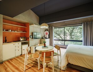 Une chambre d’hôtel moderne dotée d’un coin repas, d’un lit et d’une grande fenêtre donnant sur la verdure.