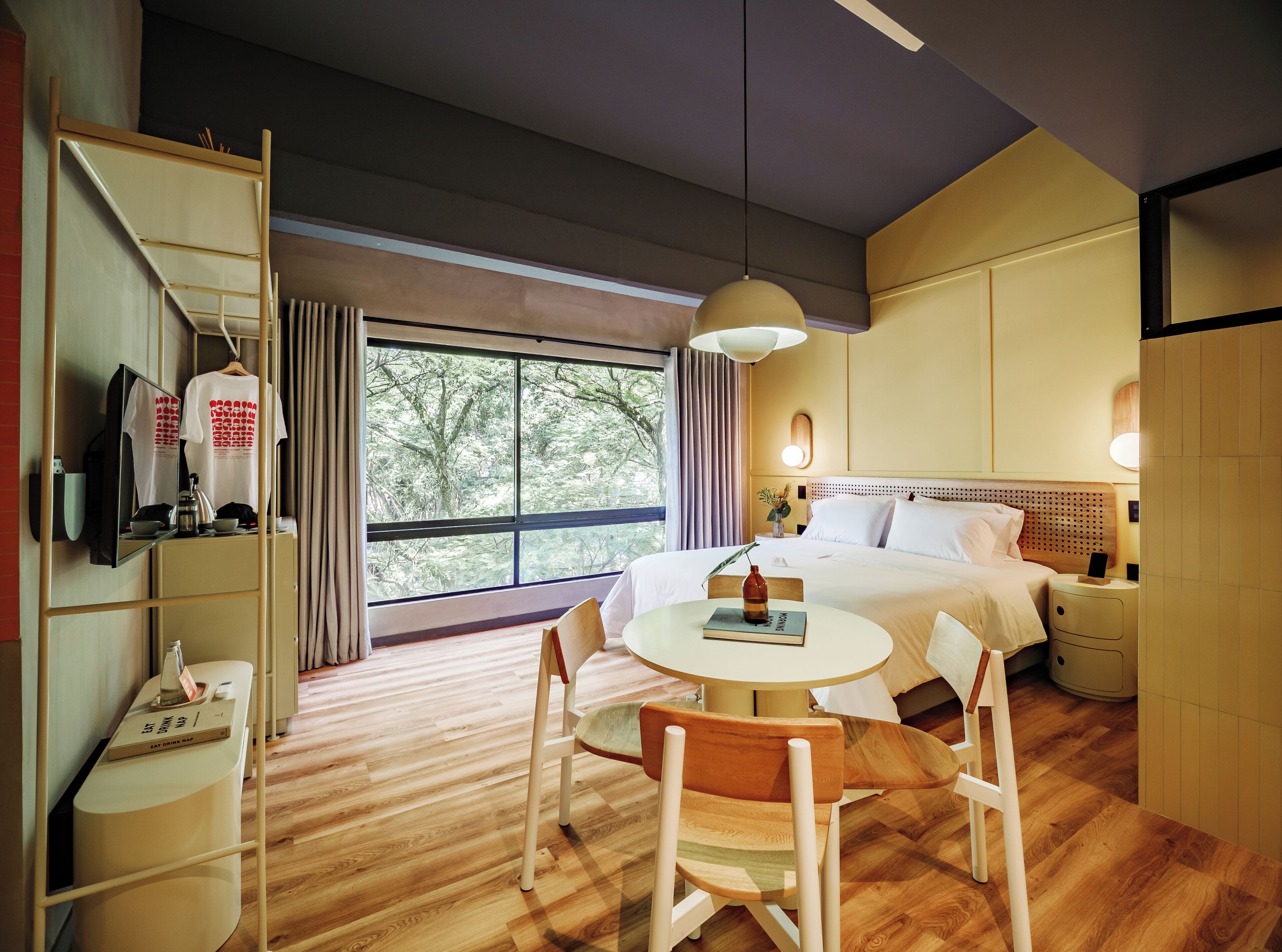 Habitación de hotel con cama, mesita de noche, lámpara, silla y escritorio con espejo y televisor.