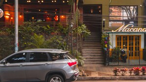 A multi-story building with a restaurant named "Macana" on the ground floor. There is a car parked in front, and the building is surrounded by greenery. - The Somos Flats Provenza (Medellín)
