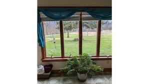 A room with a large window, a potted plant, and a bench with cushions. - Your summer getaway- with a hot tub!

 (Millmont)