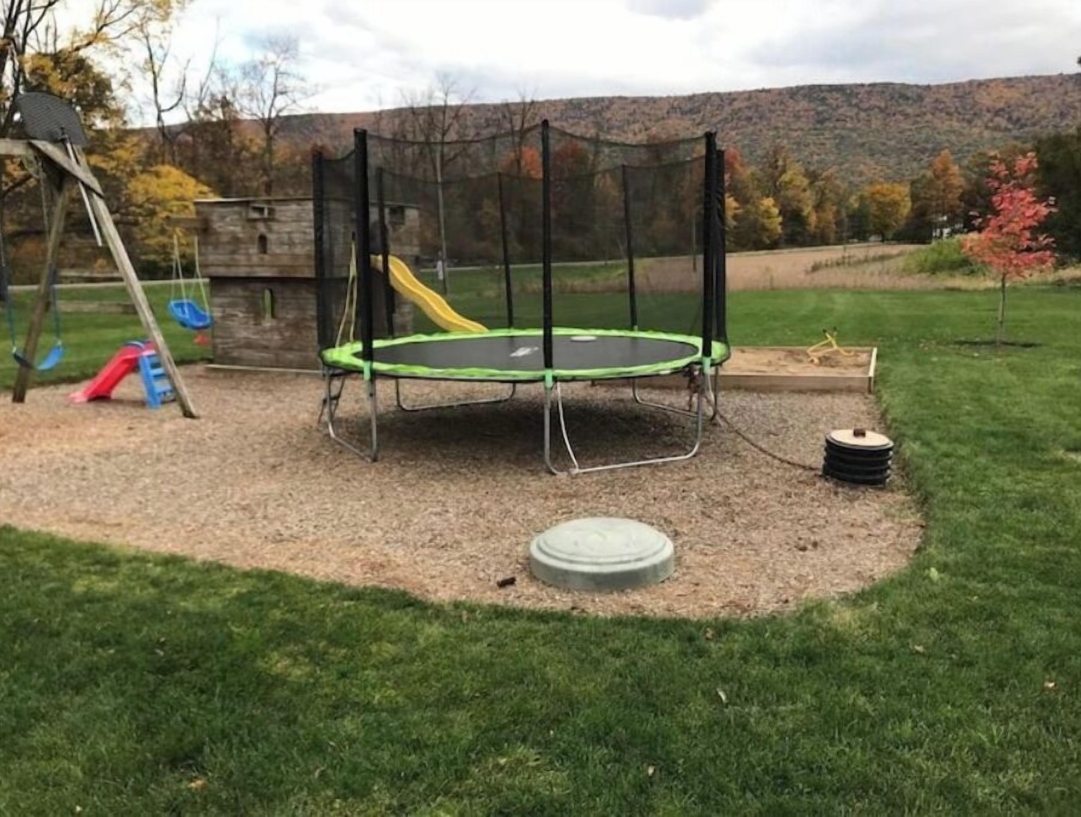 A trampoline in a backyard with a swing set and a slide.